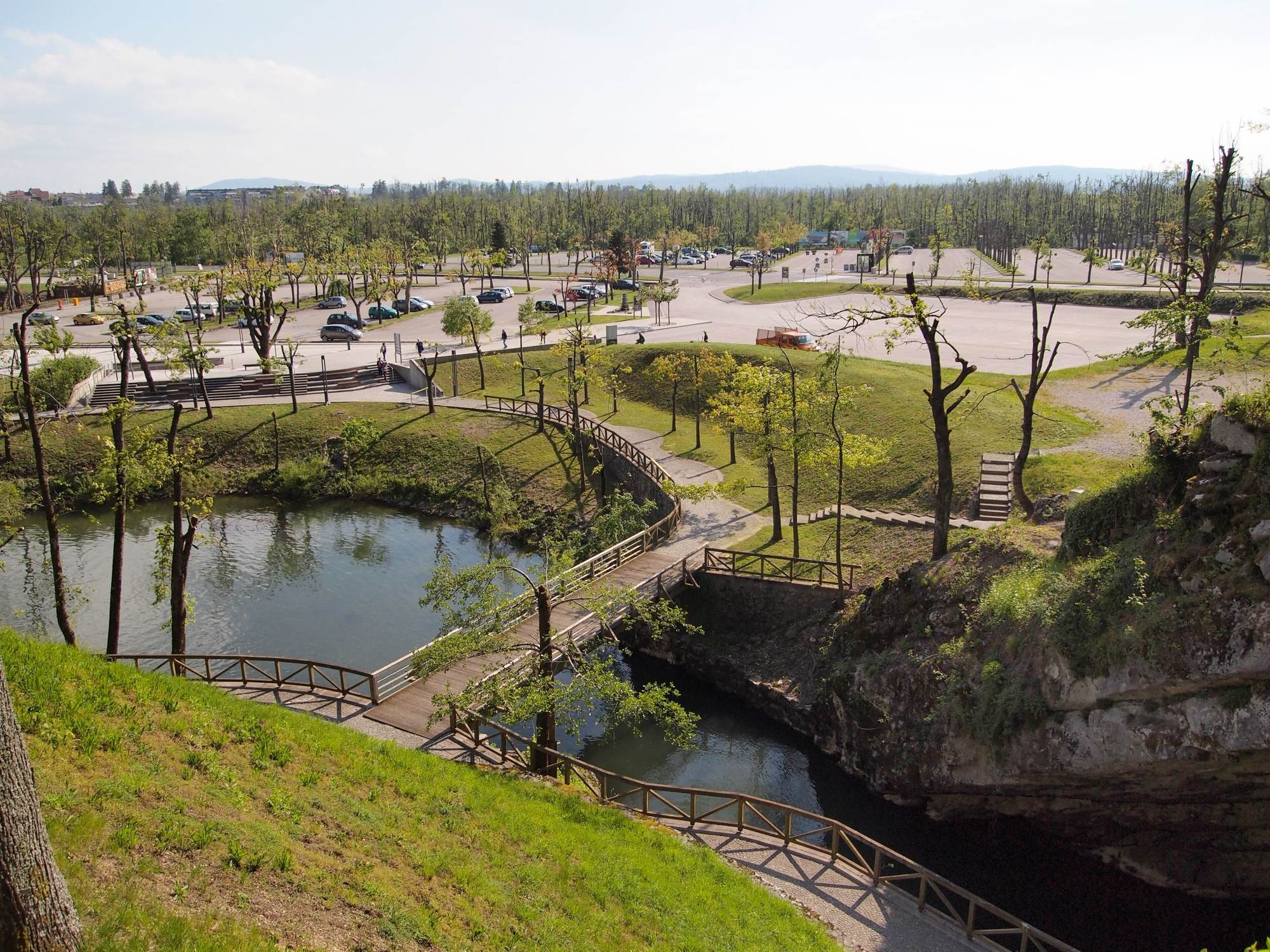 The park outside Postojna Cave: footbridges over the Pivka river, lawns and the large visitor car park